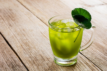 Closeup glass of Gotu Kola ice tea with green leaves ( Asiatic pennywort, Indian pennywort, Centella asiatica ) isolated on wood table background. Tropical medical herbal plant, healthy drink concept 