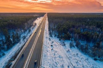 Aerial view of straight highway and pine forest in winter at sunset. View from above