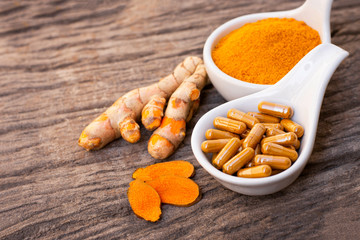Turmeric ( curcumin, Curcuma ) powder and tumeric capsule isolated on wood background. Supplement concept. Top view. 
