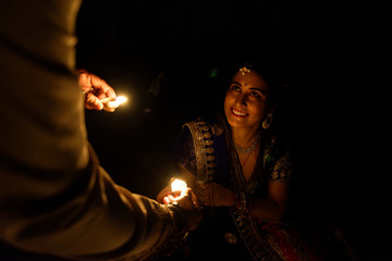 Beautiful Indian Gujarati couple in Indian traditional dress lightening Diwali diya/lamps sitting on the floor in darkness on Diwali evening. Indian lifestyle and Diwali celebration