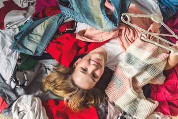 Fast fashion, Girl lies on a bunch of colorful clothes in the dressing room. Concept of recycling,...