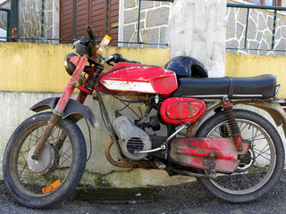 Naklejka na ściany i meble Old red with chrome motorcycle parked near the old buildings. Old red motorcycle with rust 