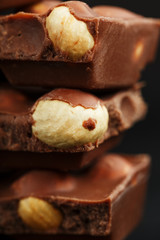 Chocolate with hazelnut in the form of a tower on a dark background. Pieces of milk chocolate with nuts.