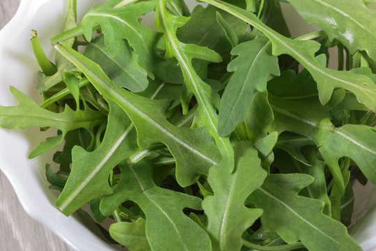 Fresh Rucola leaves in the bowl on a wooden background. Vegan food.