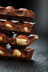 Chocolate with hazelnut in the form of a tower on a dark background. Pieces of milk chocolate with nuts.