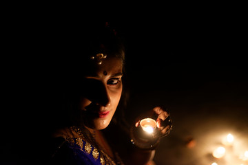 Young and beautiful Indian Gujarati woman in Indian traditional dress celebrating Diwali with illuminated diya/lamps on rooftop on Diwali evening. Indian lifestyle and Diwali celebration