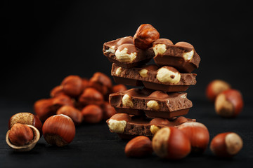 Chocolate with hazelnuts in the form of a tower on a dark background, surrounded by nuts in the...