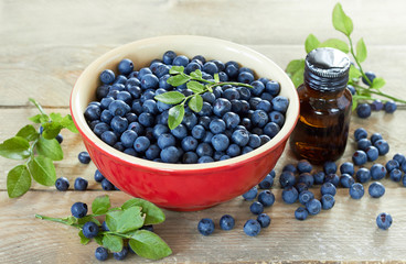 Blueberry in a red bowl with leaf on top on wooden table