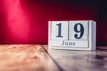 June 19th. Day 19 of month, calendar on business office table, workplace with vivid maroon red background. Summer time