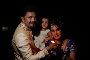 Young and beautiful Indian Gujarati father,mother and kid in traditional dress celebrating Diwali with diya/lamps on the terrace in darness  on Diwali evening. Indian lifestyle and Diwali celebration
