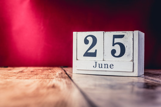 June 25th. Day 25 of month, calendar on business office table, workplace with vivid maroon red background. Summer time