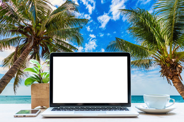 Mockup of laptop computer with empty screen with coffee cup and smartphone on table at landscape early sunrise over blue the sea background,working on the beach,Freelance work and holiday traveler.