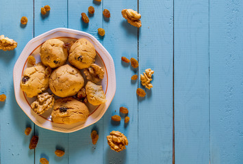 Homemade walnut and raisin cookies in a plate. Top view of cookies on table with scattered raisins and walnuts. Copy space for text.