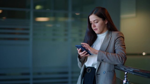 Beautiful girl with dark hair sends a message on her smartphone. She's in the office.
