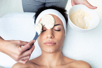 Cosmetologist applying the alginates facial mask to woman on the spa center.