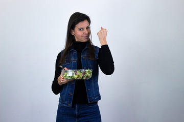 "Portrait of rich attractive caucasian middle age woman with salad., isolated on gray background studio shot, black sweater, denim jacket, jeans, dark air. Place for your text in copy space."