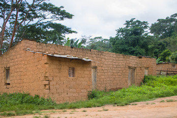 Fototapeta na wymiar View of traditional village, thatched and zinc sheet on roof houses and terracotta brick walls, cloudy sky as background, in Angola
