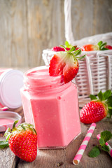 Strawberry milkshake in bottles, with fresh strawberries and mint on sunlight summer wooden and glass background, copy space