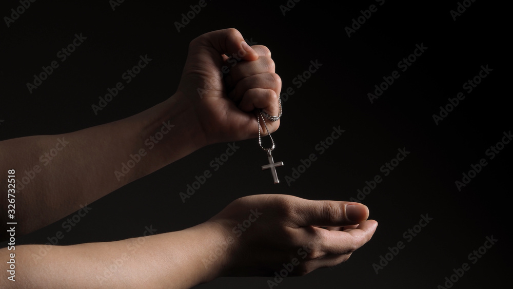 Wall mural Silver crucifix or cross pendant and necklace on body or hand studio shot black color background which represent to praying for god or jesus for christian religion people who have faith