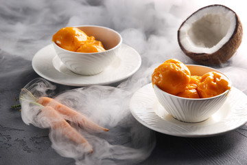 Desserts. Fruit ice cream in a white bowl next to coconut and carrots. White smoke. Background image, copy space