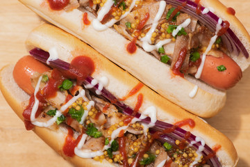 top view of delicious hot dogs with red onion, bacon and Dijon mustard on wooden table