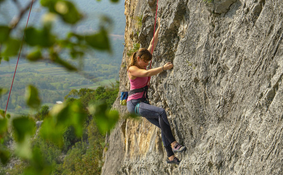 CLOSE UP: Young female rock climber scales a massive cliff on a sunny day.