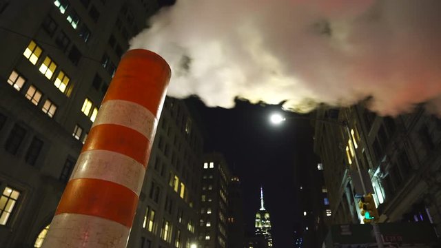 Steam rises and drifts among the rows of buildings along the Fifth Avenue at front of Empire State Building in the night at New York City NY USA during the Christmas Holidays seasons on Dec. 2018.