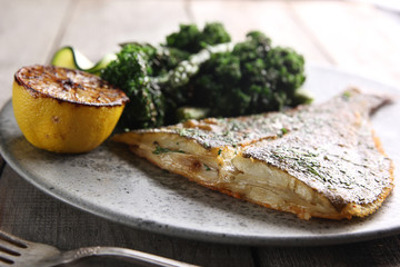 Seafood. Fried flounder with asparagus, lemon and cabbage on a light wooden background. Fish with vegetables. Background image, copy space