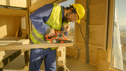 CLOSE UP: Young builder working on a prefabricated house sands a wooden beam.