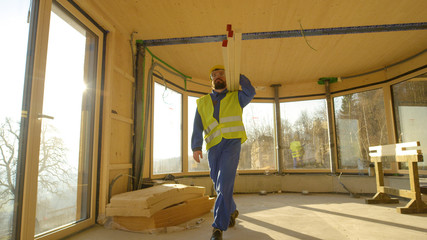 LOW ANGLE: Worker arrives to work carrying heavy wooden beams on his shoulder