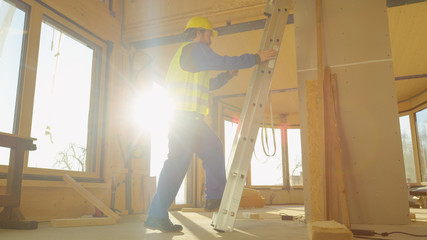 LOW ANGLE: Builder climbs up a stepladder placed inside prefabricated house