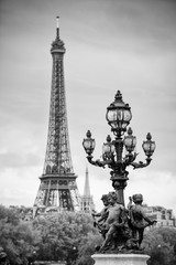 Fototapeta na wymiar Scenic postcard view in Paris, France with statues of cherubs on an Art Nouveau street lamp on the Pont Alexandre III Bridge with the Eiffel Tower standing in black and white monochrome