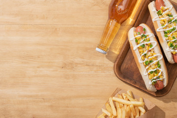 top view of delicious hot dogs with corn, green onion and mayonnaise near french fries and beer on wooden table