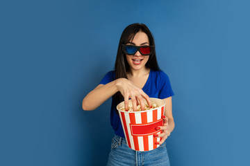 Emotional watching cinema. Beautiful caucasian woman's portrait on blue studio background. Beautiful female brunette model. Concept of human emotions, facial expression, sales, ad, copyspace.