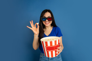 Obraz premium Emotional watching cinema. Beautiful caucasian woman's portrait on blue studio background. Beautiful female brunette model. Concept of human emotions, facial expression, sales, ad, copyspace.