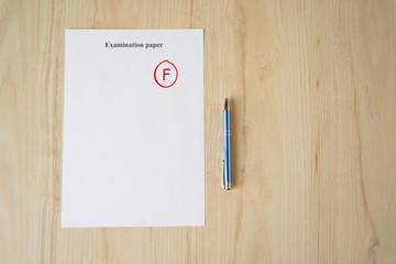 Examination paper with grade test results. Failed university exam with pen on the school desk....