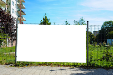 Blank white banner for advertisement on the fence. Residential area on a sunny summer day.