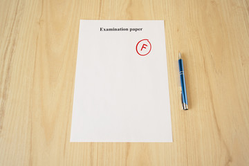 Examination paper with grade test results. Failed university exam with pen on the school desk....