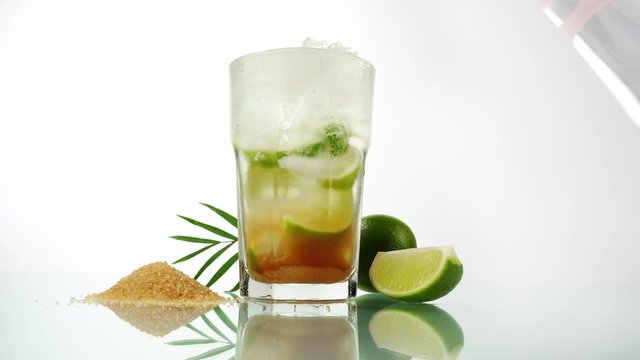 Pouring Cachaca in a Caipirinha Cocktail on white Background - Lime and brown Sugar