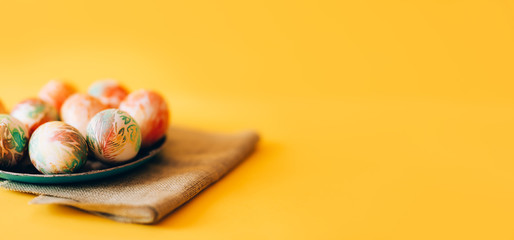 Easter eggs with ornament on green plate with napkin on yellow background