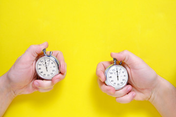 Mechanical stopwatches in two hands on a yellow background.