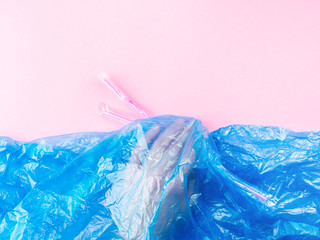 Plastic straws being thrown in ocean represented by blue plastic bag and hand under water. Pollution concept on pink background.