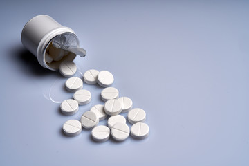 White tablets are scattered from a bottle on a gray background. Medicine concept.