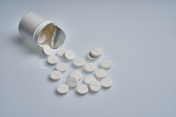 White tablets are scattered from a bottle on a gray background.