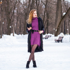 Full-length portrait of a young woman in black long down jacket posing in winter park