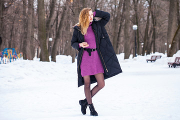 Full-length portrait of a young woman in black long down jacket posing in winter park