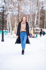Fototapeta na wymiar Full-length portrait of a young woman in black long down jacket posing in winter park