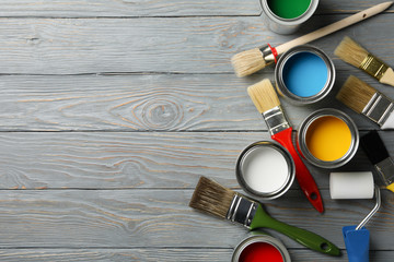 Different paints, brushes and roller on wooden background, top view