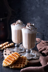 Two cups of coffee with whipped cream and grated chocolate on a dark concrete background. Viennese coffee with Viennese waffles.