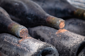 Closeup dark dusty wine bottles with old crumbly cork. Long aging, musty winery vault, rare ancient collection, cork worm